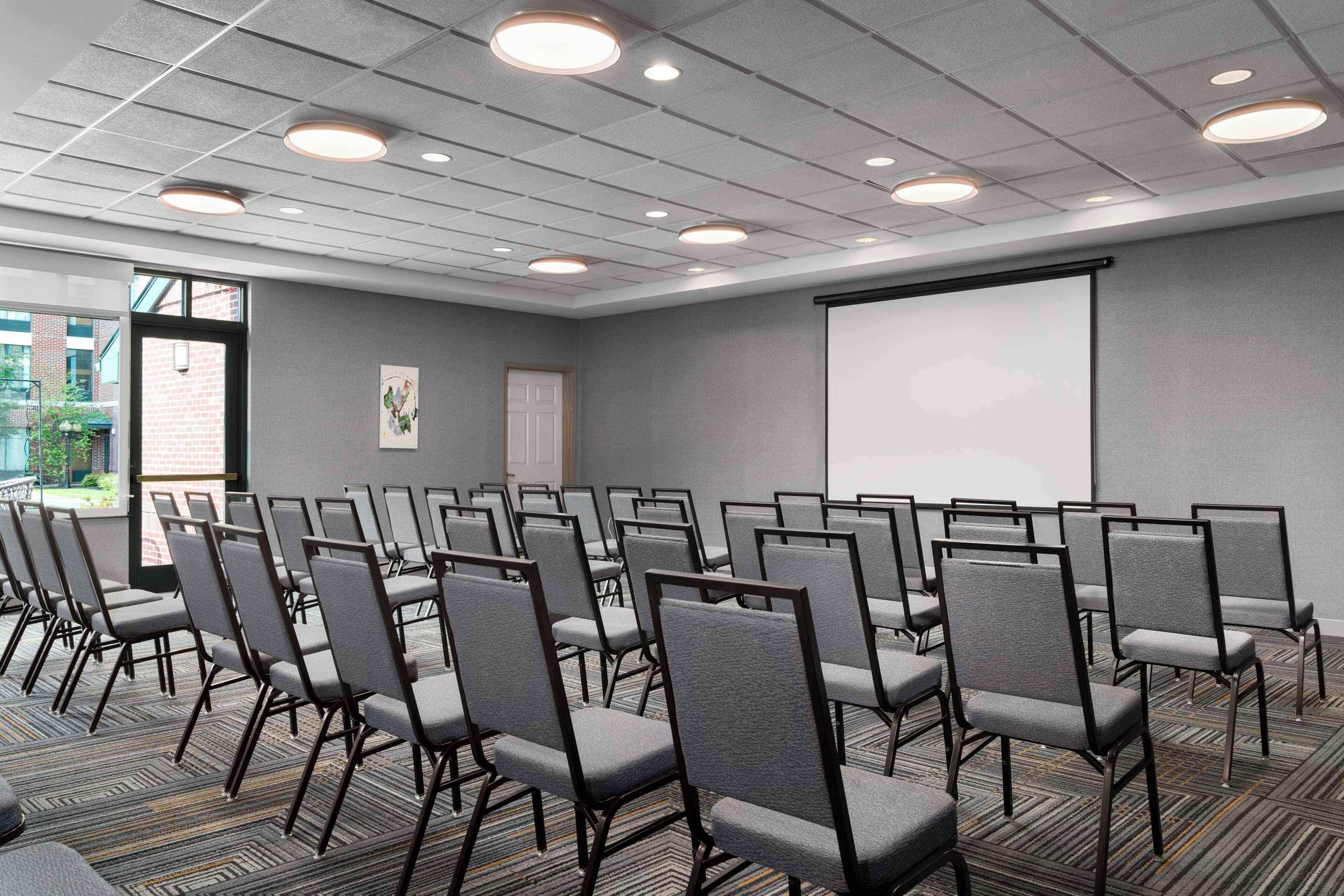 A conference room with rows of chairs, a projector screen, and a door leading outside.