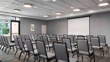 A conference room with rows of chairs, a projector screen, and a door leading outside.