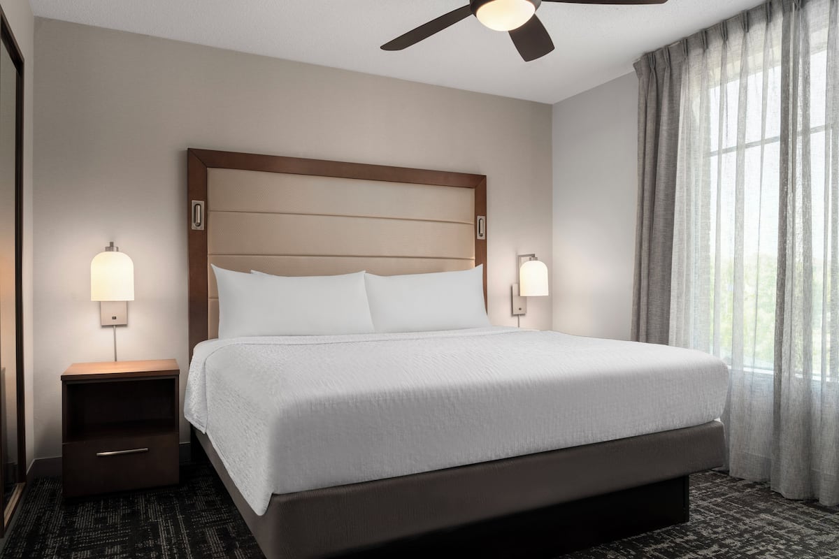 Une chambre d’hôtel avec un grand lit, deux lampes de chevet, un ventilateur de plafond et une fenêtre avec des rideaux.