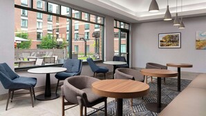 A modern indoor seating area with round tables and chairs, large windows offering a view of a brick building and greenery outside. - Homewood Suites by Hilton-Hartford South-Glastonbury, CT (Glastonbury)