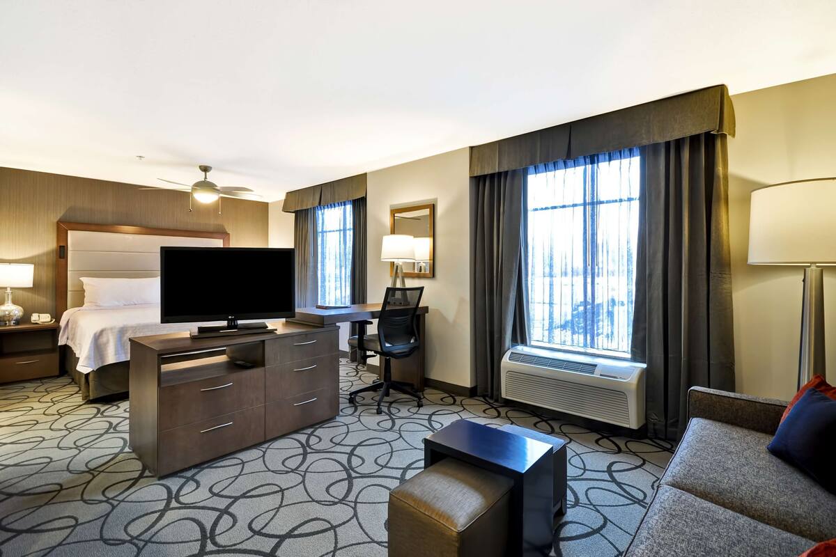 A hotel room with a bed, TV, desk, chair, and a sofa.