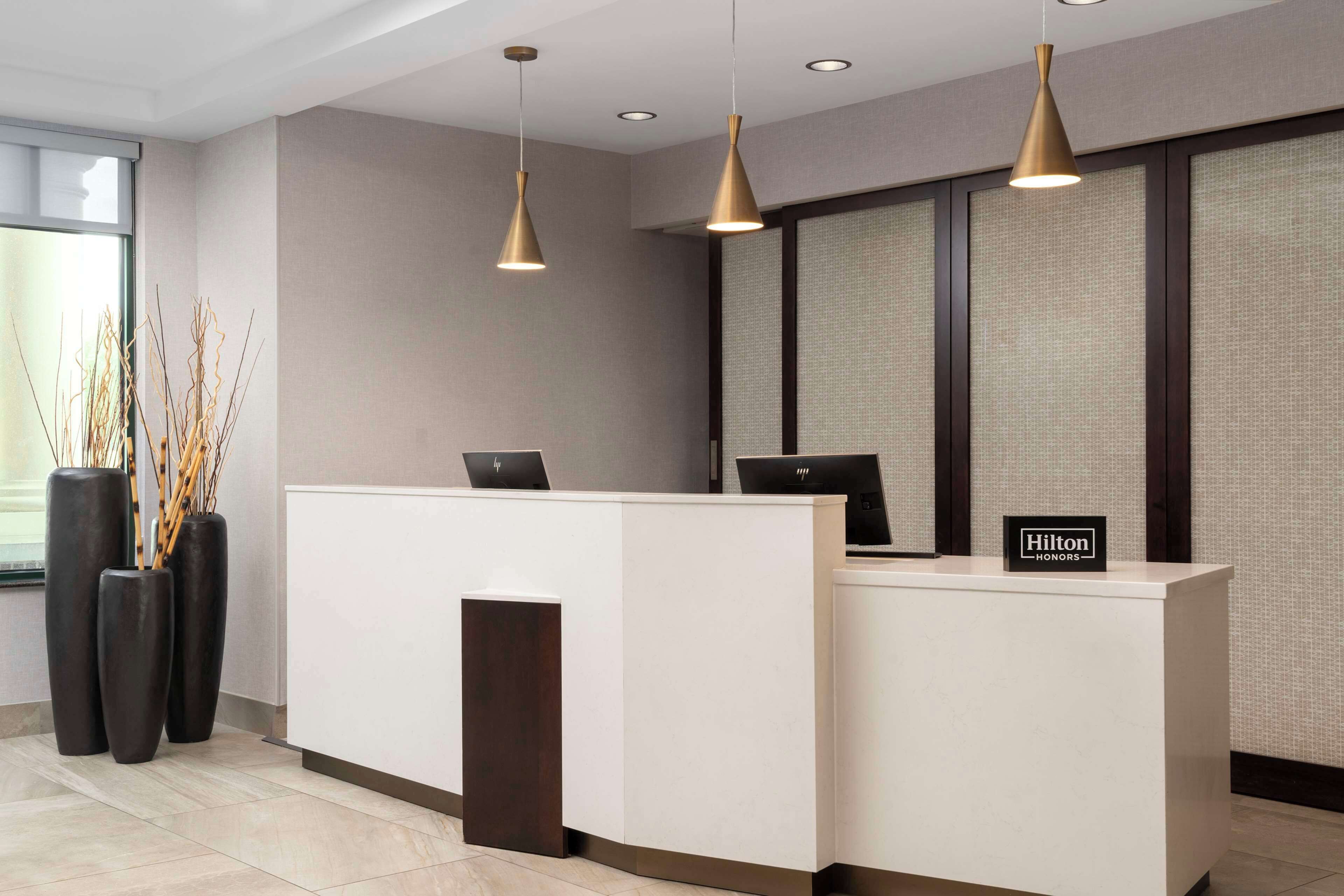 A modern hotel reception desk with two pendant lights, a large window, and a sign indicating 'Hilton Honors'.