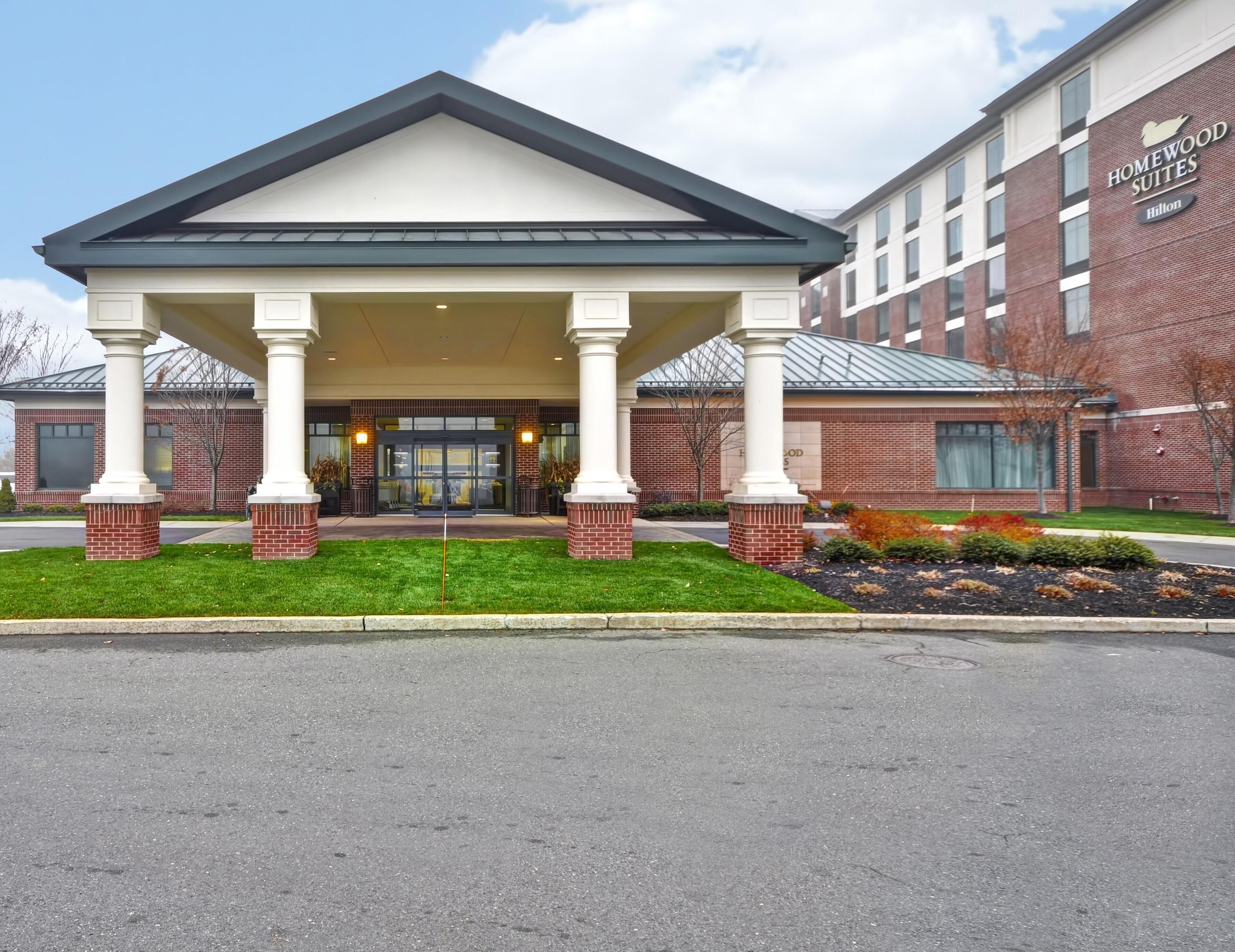 Entrada de un hotel con un porche cubierto, fachada de ladrillo y un letrero de Homewood Suites Hilton.