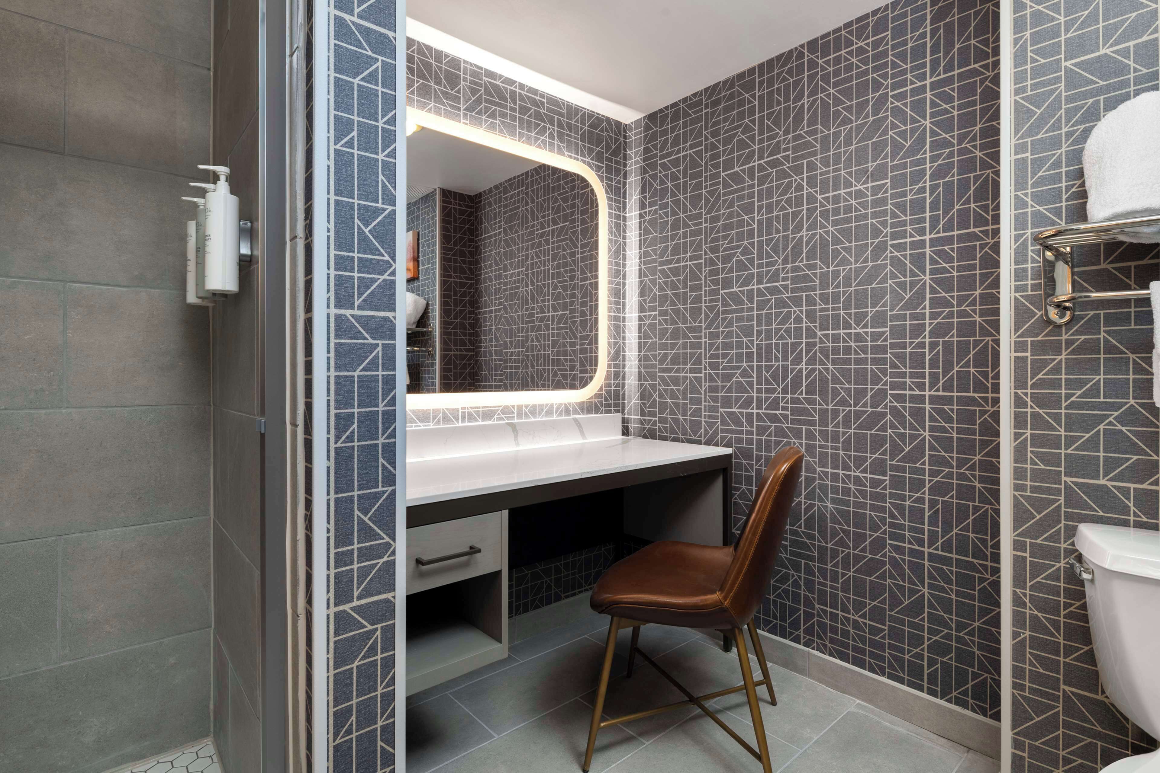Une salle de bain comprenant un meuble-lavabo, une chaise, des toilettes et un espace douche.