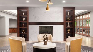A spacious living room with a fireplace, two armchairs, a coffee table, and a large window with a view of greenery. - Homewood Suites by Hilton-Hartford South-Glastonbury, CT (Glastonbury)