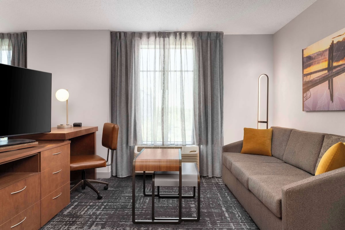 Une chambre d’hôtel avec un bureau en bois, une télévision, un canapé et un tableau au mur.