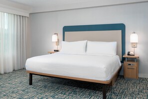 Habitación de hotel con cama, dos mesitas de noche con lámparas, una mesita auxiliar y suelo alfombrado.