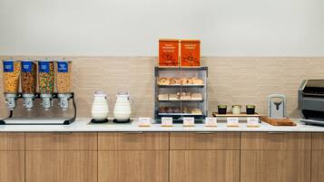 Un comptoir pour le petit-déjeuner avec des distributeurs de céréales, une machine à café, des pots à lait et un présentoir de viennoiseries.
