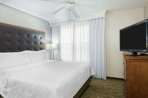 A hotel room with a large bed, a ceiling fan, a TV on a wooden cabinet, and a window with sheer curtains. - Homewood Suites by Hilton Holyoke-Springfield/North (Holyoke)