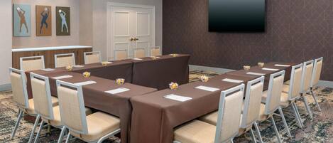 A conference room with a long table, chairs, a television, and artwork on the wall.