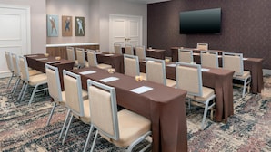 A conference room with multiple tables and chairs, a flat-screen TV on the wall, and a patterned carpet. - Homewood Suites by Hilton Holyoke-Springfield/North (Holyoke)