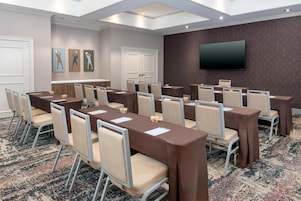 A conference room with multiple tables and chairs, a flat-screen TV on the wall, and a patterned carpet.
