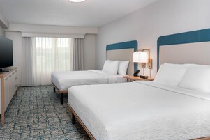 Habitación de hotel con dos camas, televisión, escritorio y ventana con cortinas.