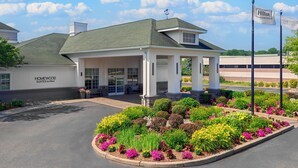 A hotel entrance with a covered patio, a garden with colorful flowers, and a clear sky. - Homewood Suites by Hilton Holyoke-Springfield/North (Holyoke)