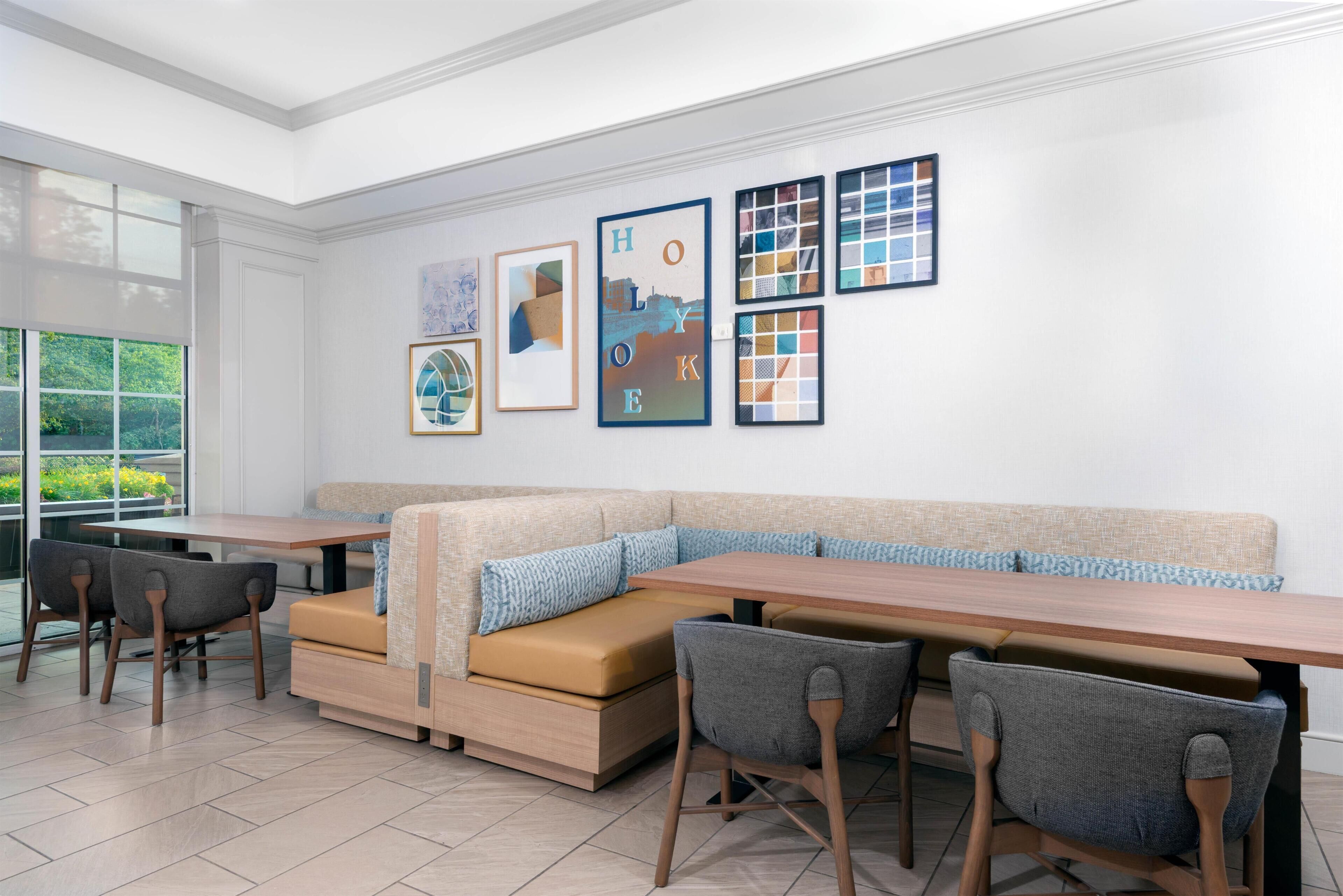 A modern dining area with a long table, cushioned seating, and framed artwork on the wall.