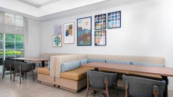 A modern dining area with a long table, cushioned seating, and framed artwork on the wall.