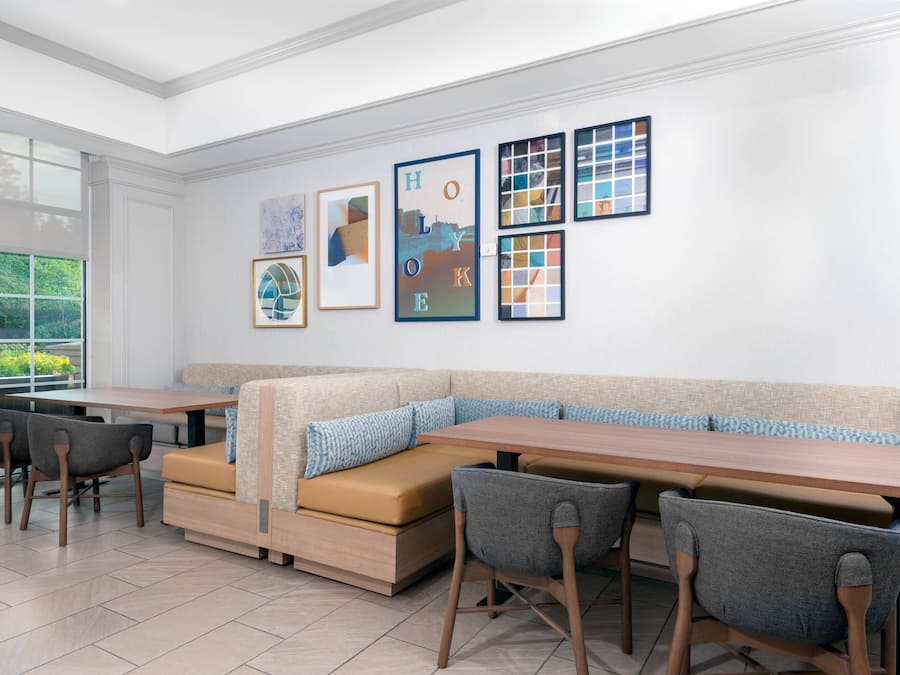 A modern dining area with a long table, cushioned seating, and framed artwork on the wall.