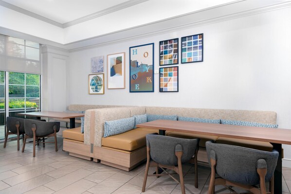 Un moderno comedor con una larga mesa, asientos acolchados y cuadros en la pared.