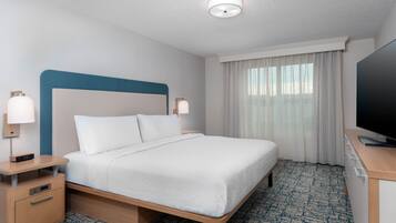 A hotel room with a bed, bedside tables, a TV, and a window with curtains.