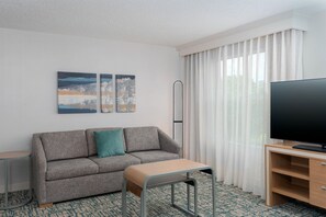 A modern hotel room with a grey sofa, a small table, a flat-screen TV, and two abstract paintings on the wall. - Homewood Suites by Hilton Holyoke-Springfield/North (Holyoke)