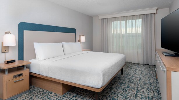 A hotel room with a bed, bedside tables, a TV, and a window with curtains. - Homewood Suites by Hilton Holyoke-Springfield/North (Holyoke)