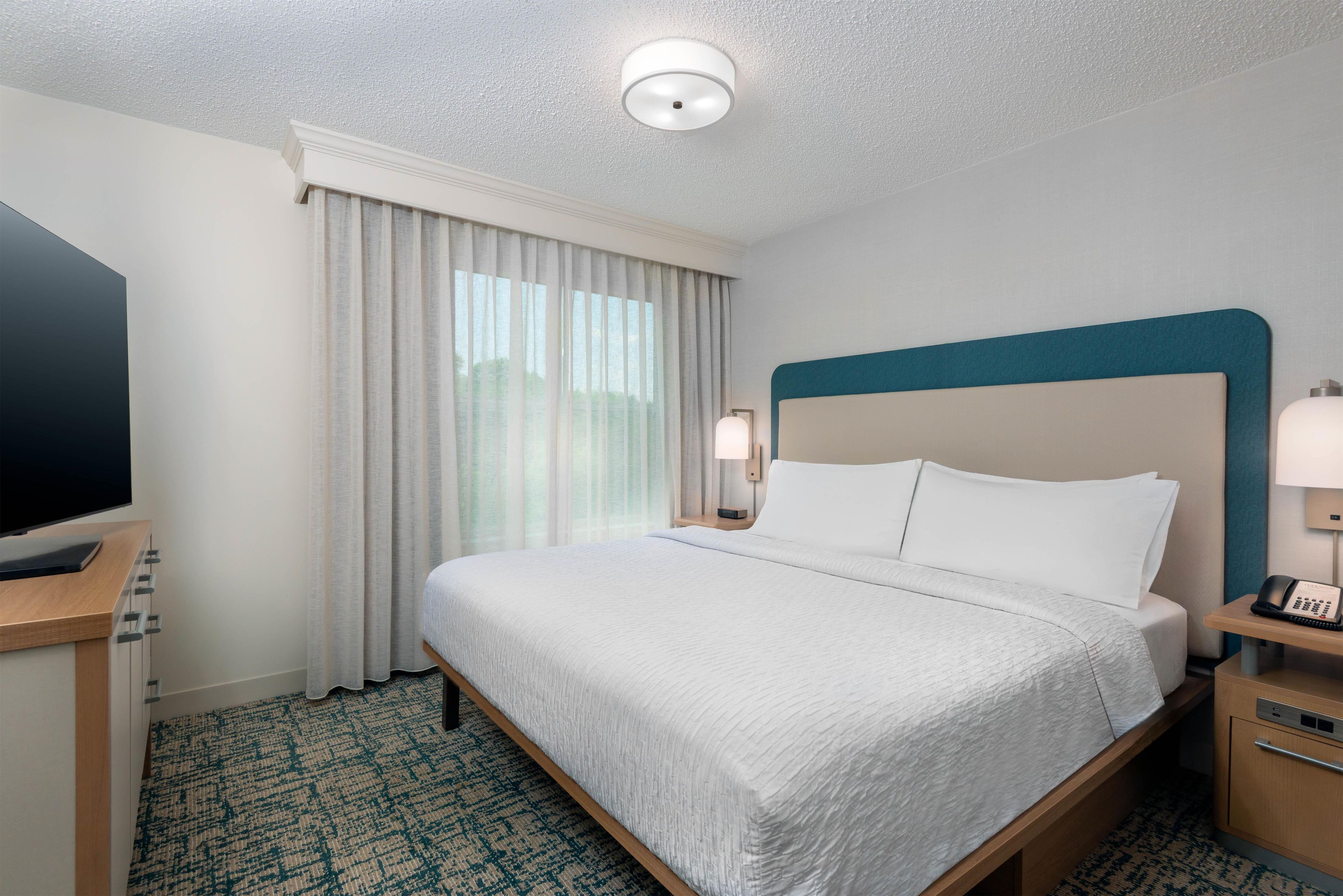 A hotel room with a bed, a television, a desk, and a nightstand.
