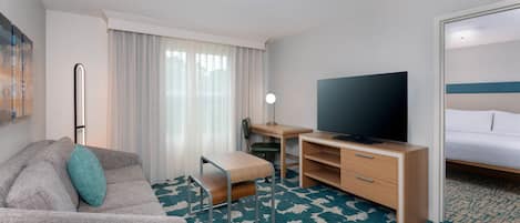 Habitación de hotel con sofá, escritorio con televisor, una silla y cama.