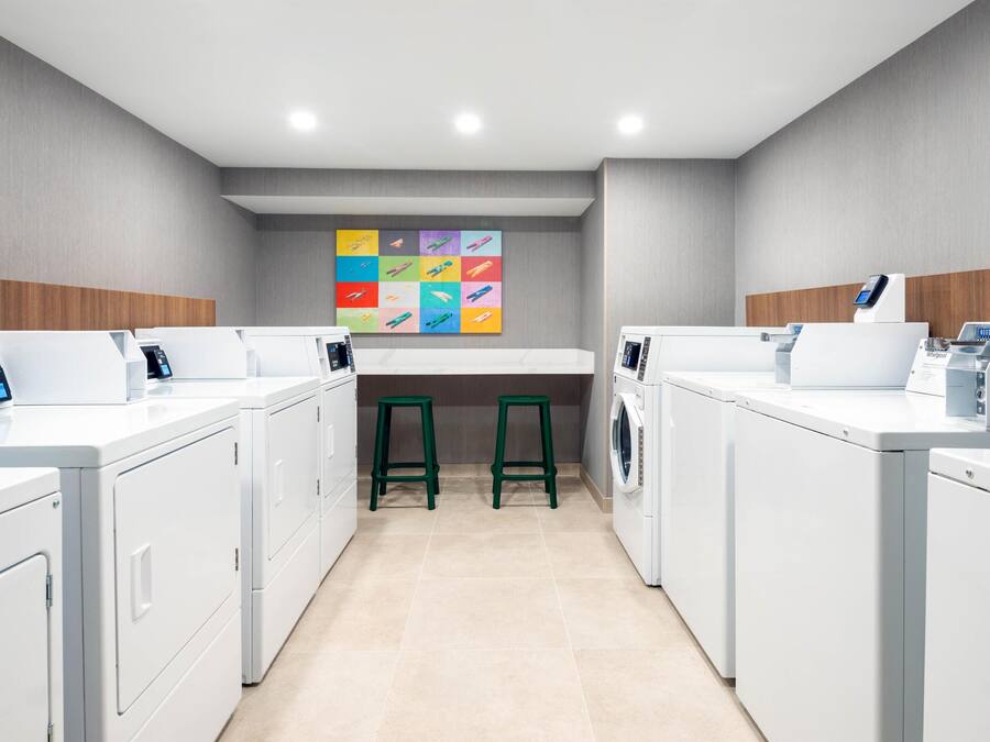 A laundry room with white appliances, green stools, and a colorful artwork on the wall.