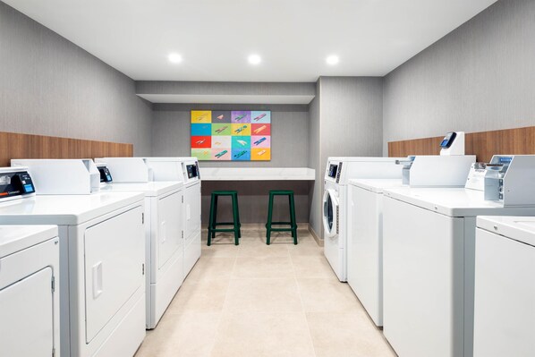 A laundry room with white appliances, green stools, and a colorful artwork on the wall.