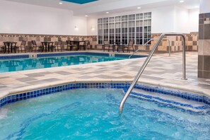 A swimming pool with a tiled edge, a metal ladder, and a tiled deck area with chairs and tables.