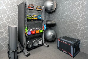 Une salle de sport équipée de divers appareils d’entraînement, notamment des kettlebells, des balles lestées et un support à squats.