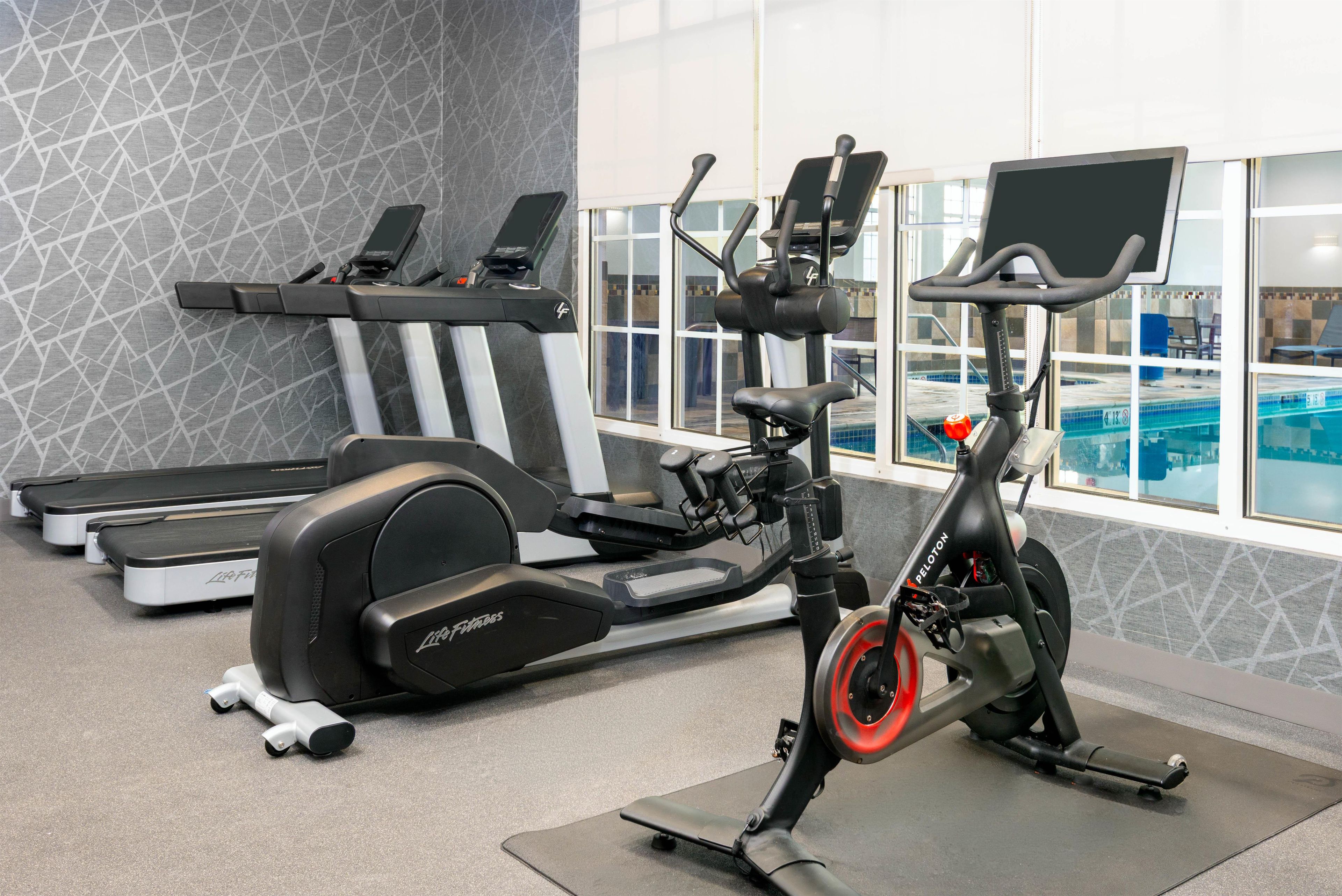 Een fitnessruimte met trainingsapparatuur, waaronder loopbanden, een elliptische trainer en een hometrainer.