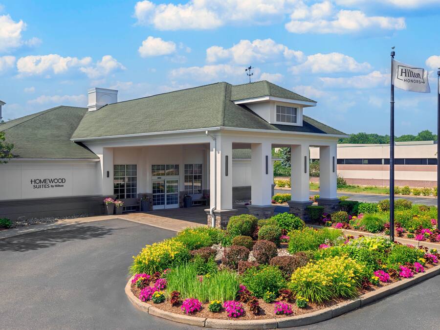 A hotel entrance with a covered patio, a garden with colorful flowers, and a clear sky.