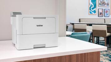 Ein Brother-Drucker auf einer weißen Theke in einer Hotelhalle mit Sitzgelegenheit und Wandbild.