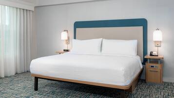 Habitación de hotel con cama, dos mesitas de noche con lámparas, una mesita auxiliar y suelo alfombrado.