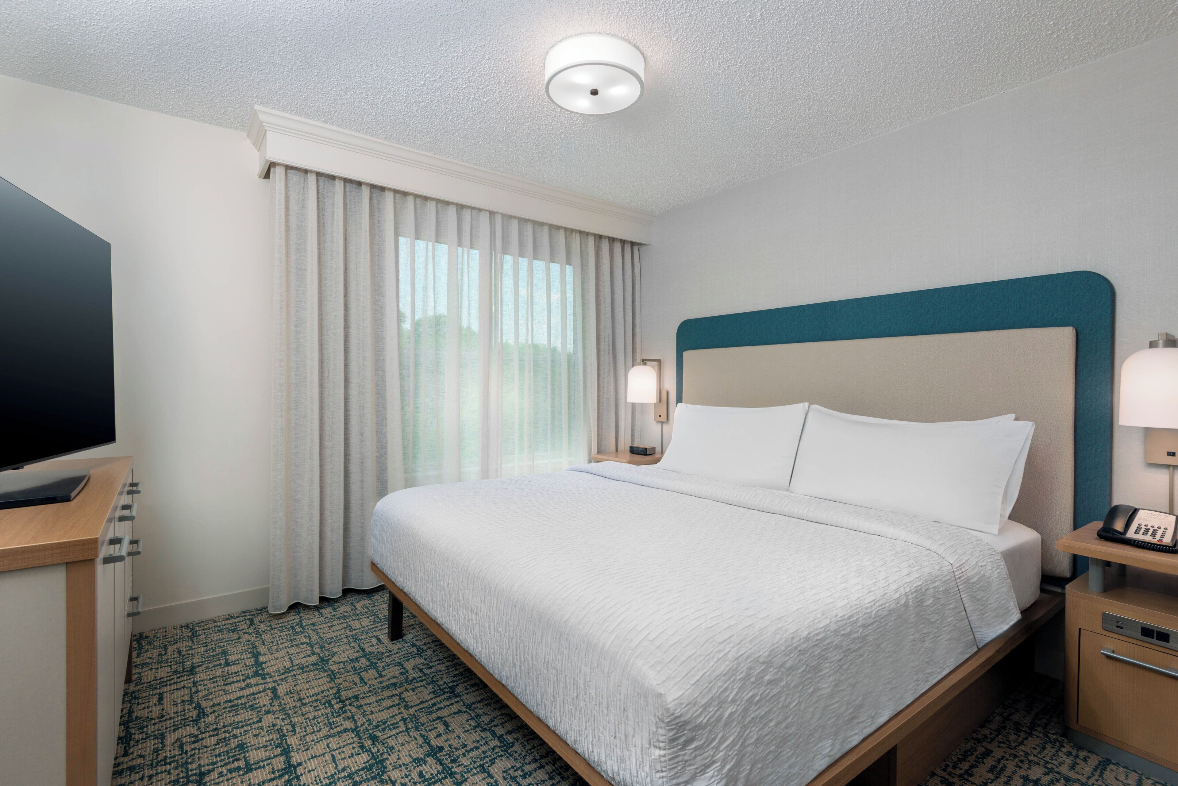 A hotel room with a bed, a television, a desk, and a telephone.