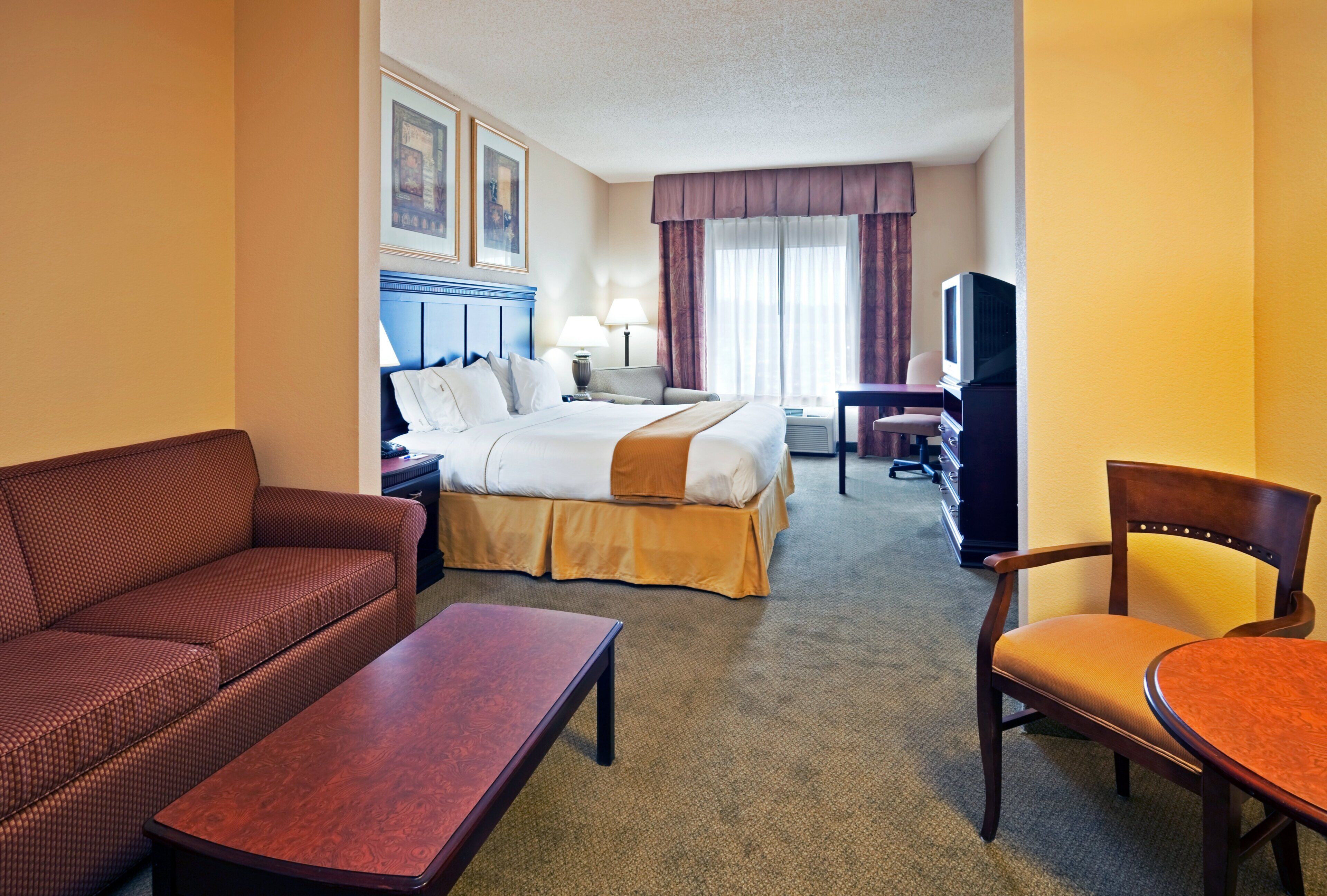 A hotel room with a bed, a sofa, a chair, a desk, and a television.