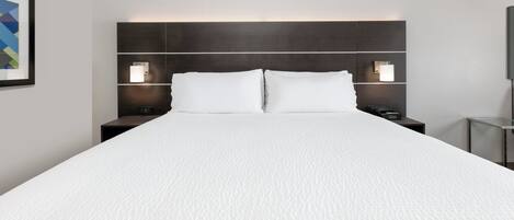 Una cama grande con cubre cama blanco texturizado, dos mesitas de noche con lámparas y un cabecero oscuro.