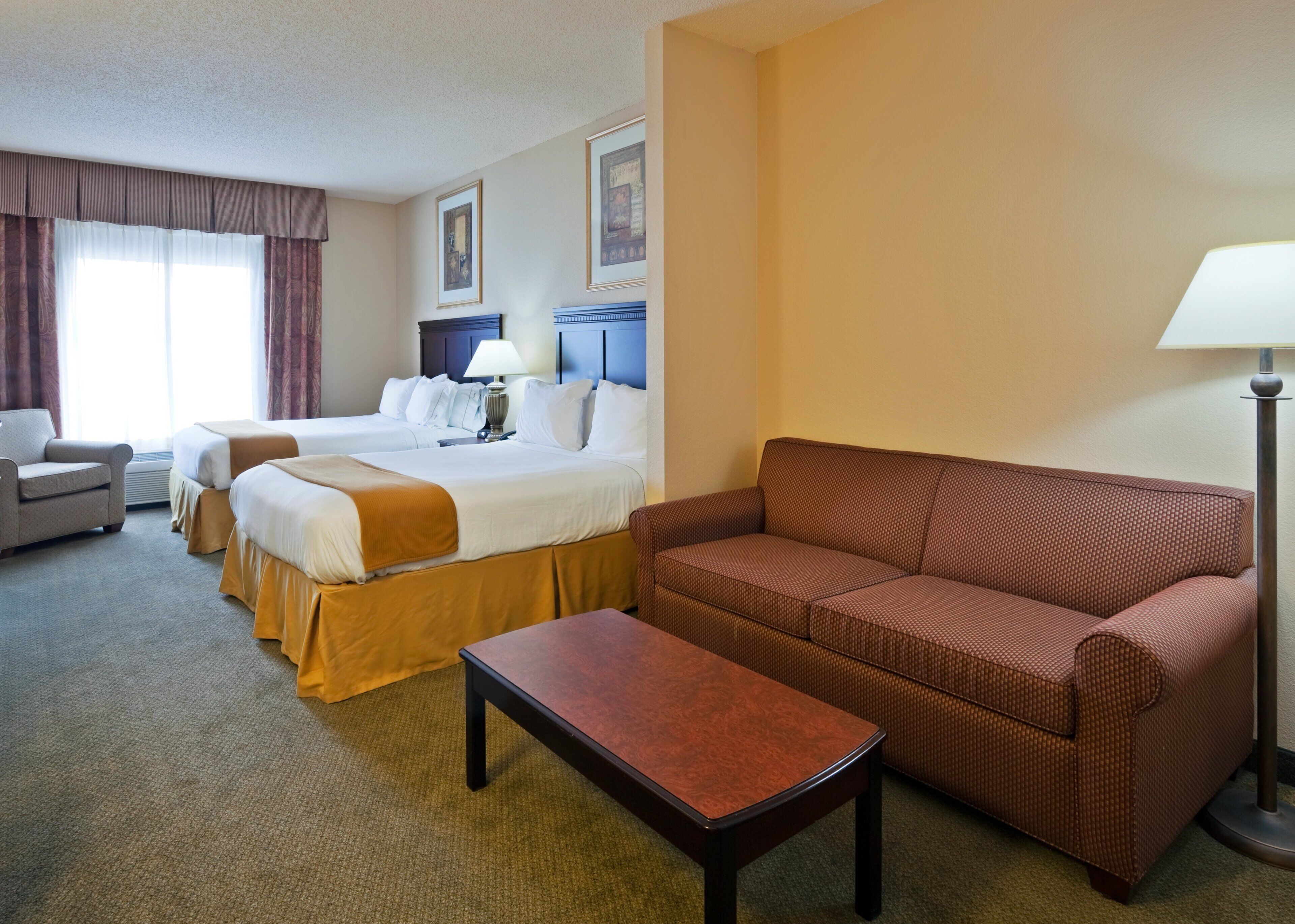A hotel room with two beds, a sofa, a chair, a table, and a lamp.
