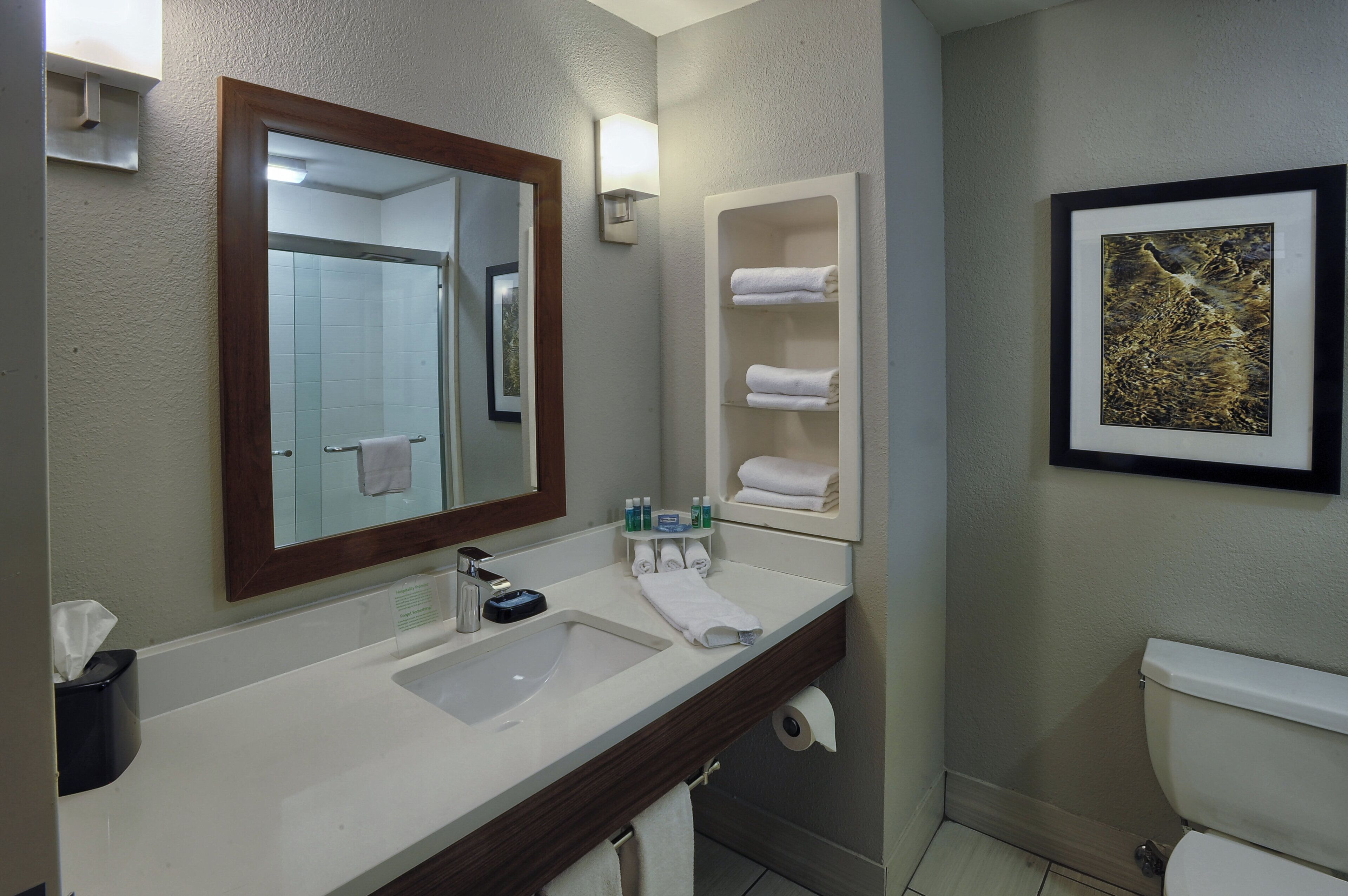 A bathroom with a large mirror, a sink, a toilet, and a shelf with towels.