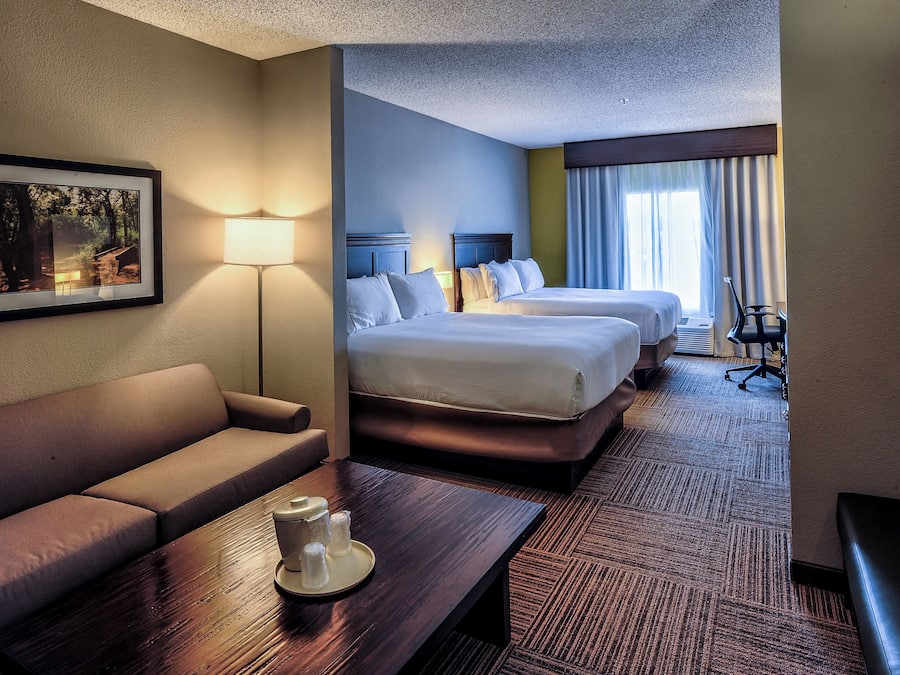 A hotel room with a sofa, a table with a tray and glasses, two beds, a desk, and a chair.