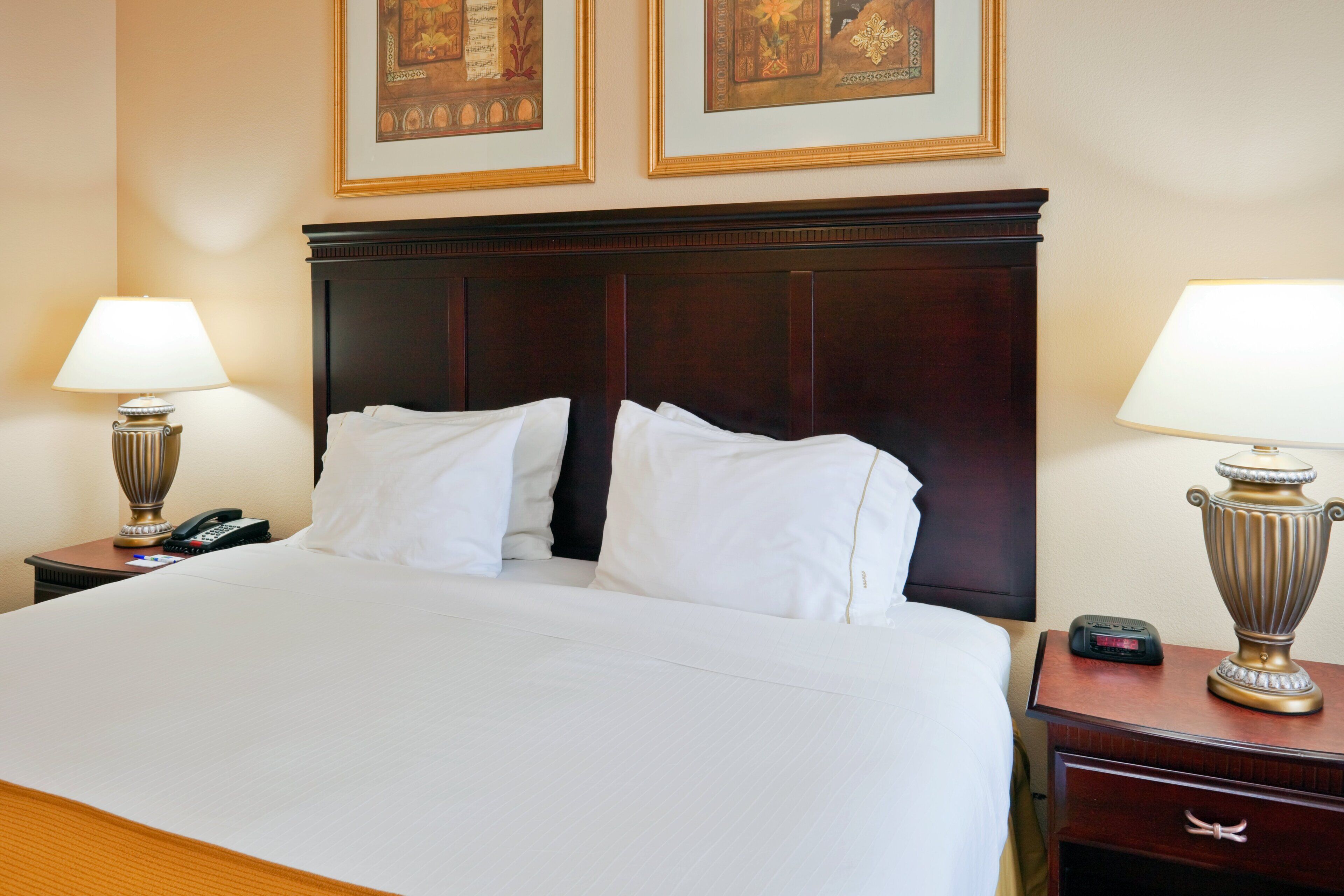 Ein Hotelzimmer mit einem großen Bett, zwei Nachttischen mit Lampen, einem Beistelltisch mit Telefon und zwei gerahmten Bildern an der Wand.