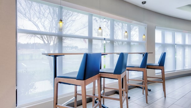 Un interior moderno con ventanas amplias, sillas de madera con cojines azules e iluminación colgante.