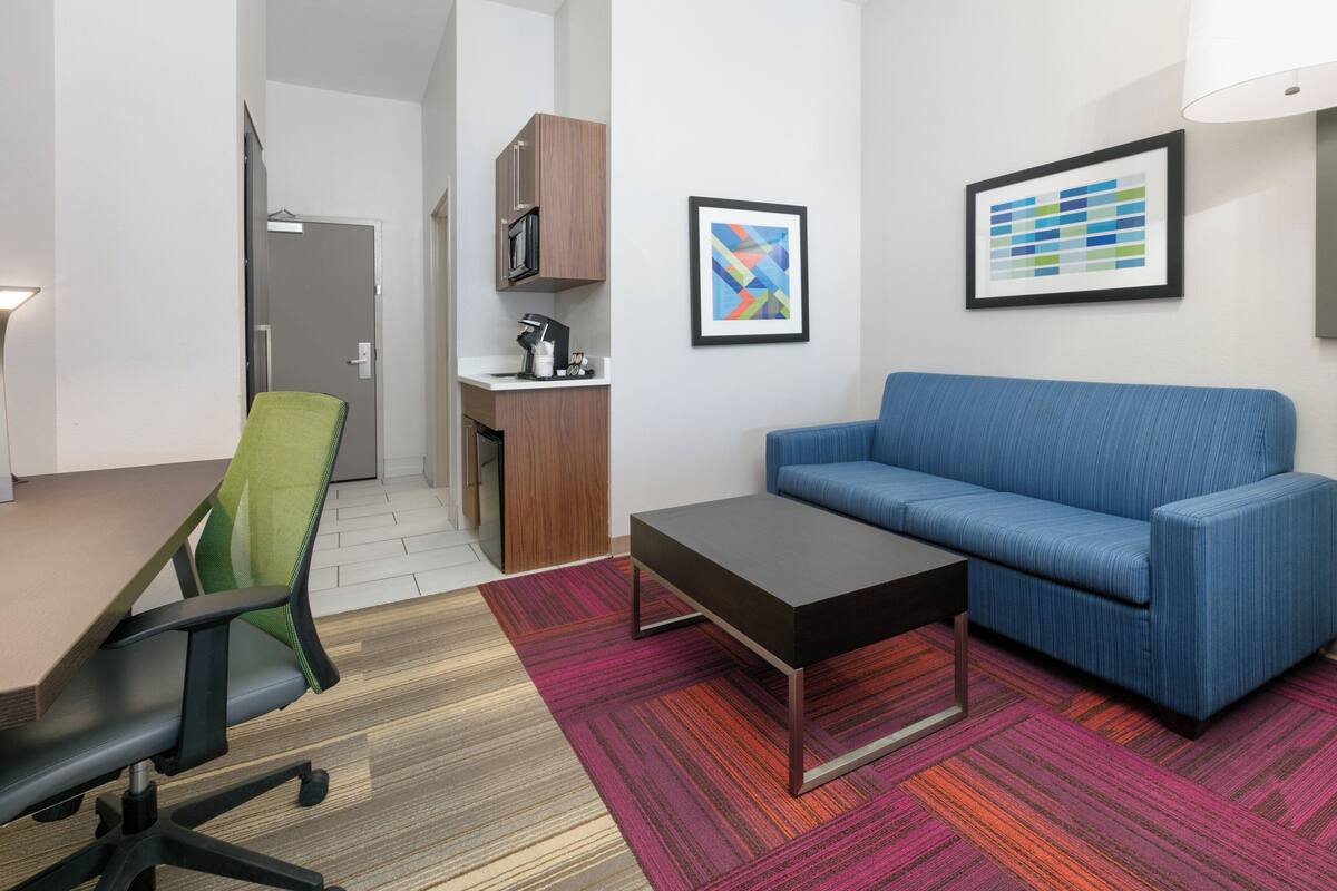 A modern office space with a green office chair, a blue sofa, a coffee table, and a kitchenette.