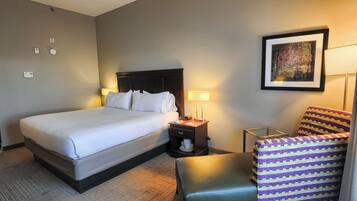 A hotel room with a bed, bedside lamps, a chair, a small table, and a painting on the wall.