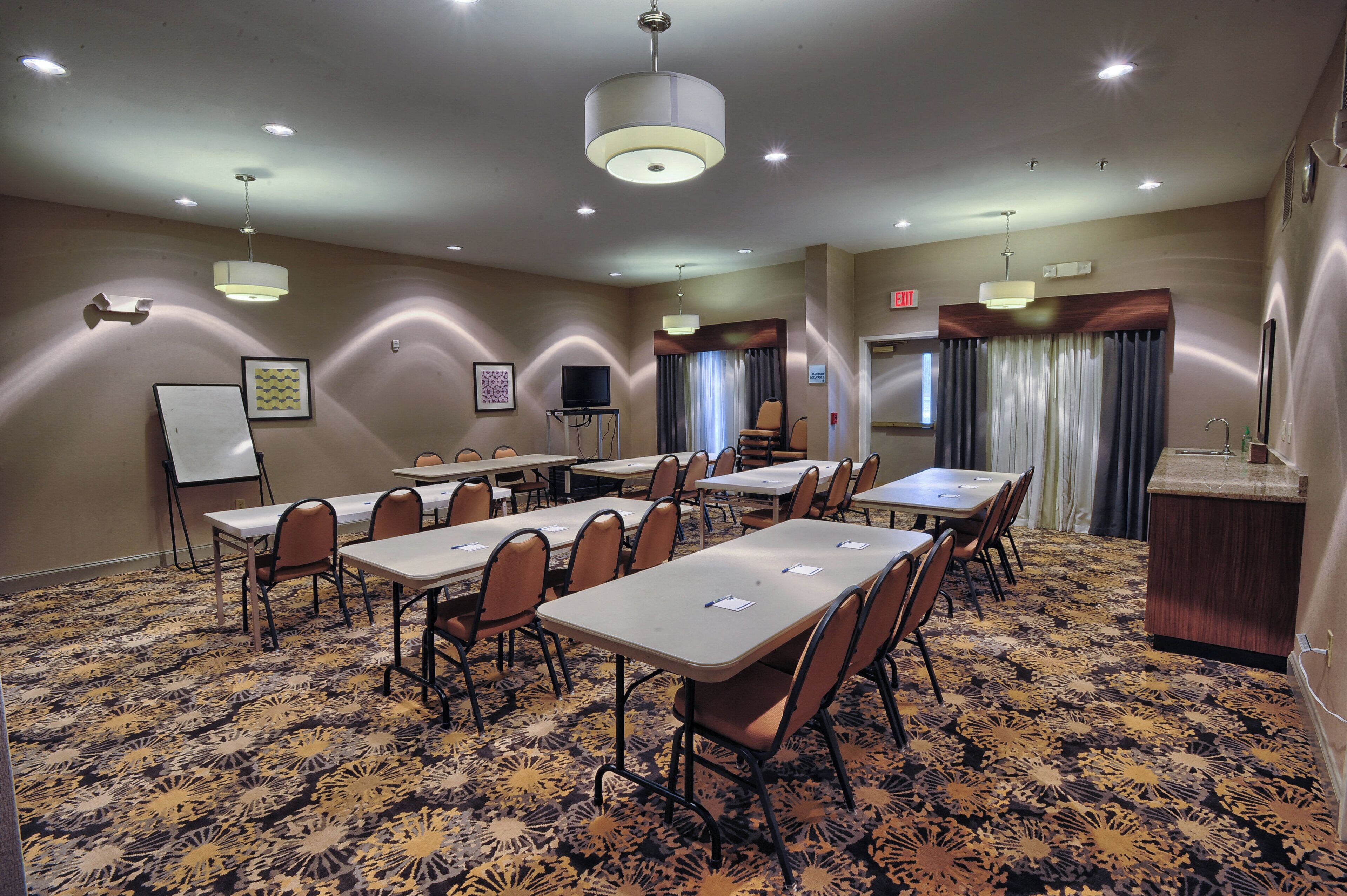 A conference room with multiple tables and chairs, a whiteboard, a television, and a reception desk.