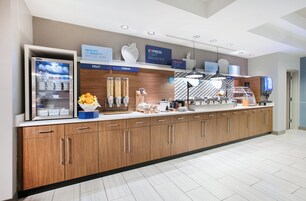 Una barra de desayuno moderna con vitrina refrigerada, opciones de cereales y fruta, y una estación de café.