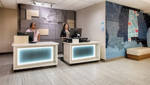 Un área de recepción con dos recepcionistas, un mostrador moderno con una computadora y una pared con diseño de mapa.