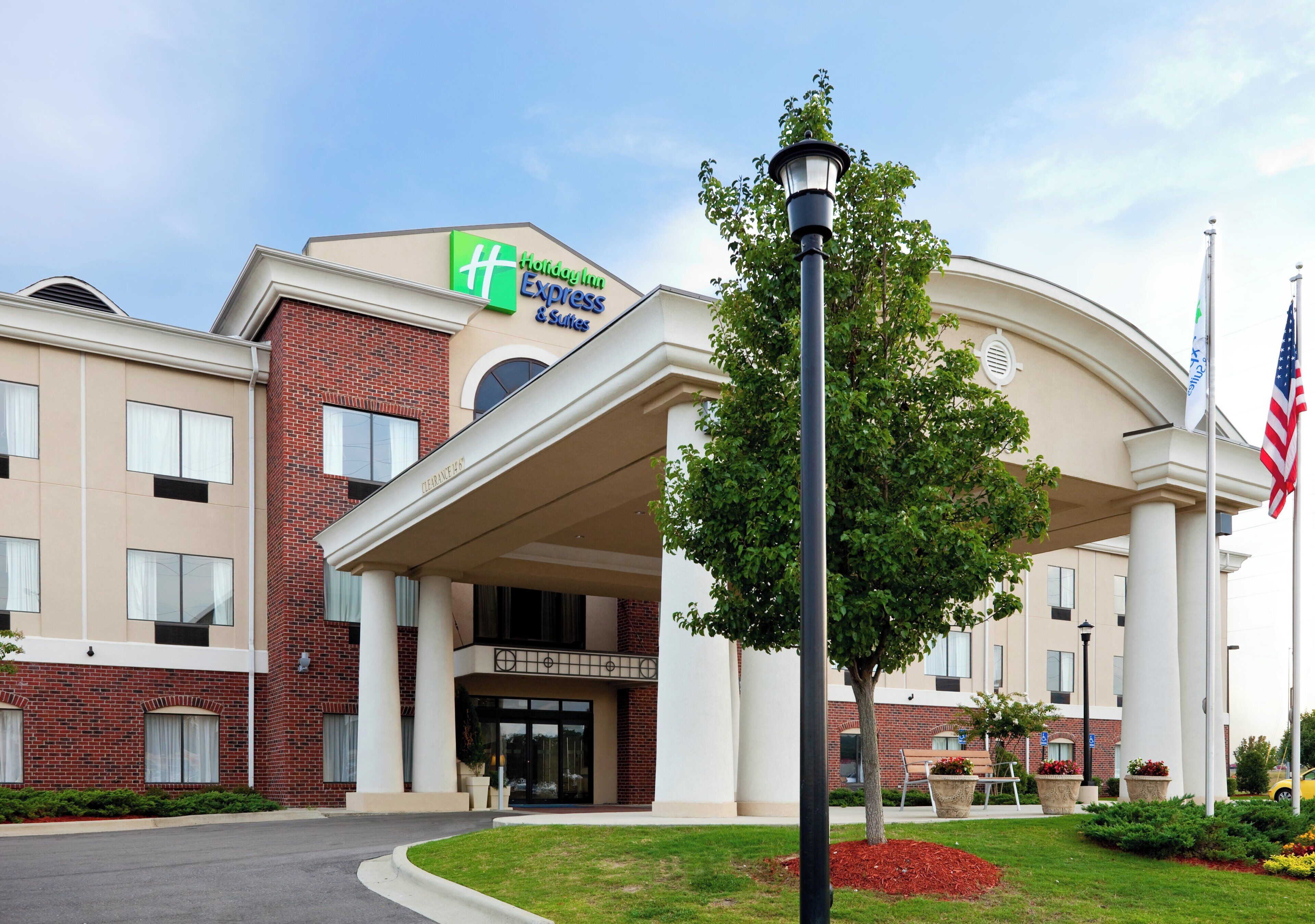 A Holiday Inn Express & Suites building with a brick facade, large entrance canopy, and American flags.