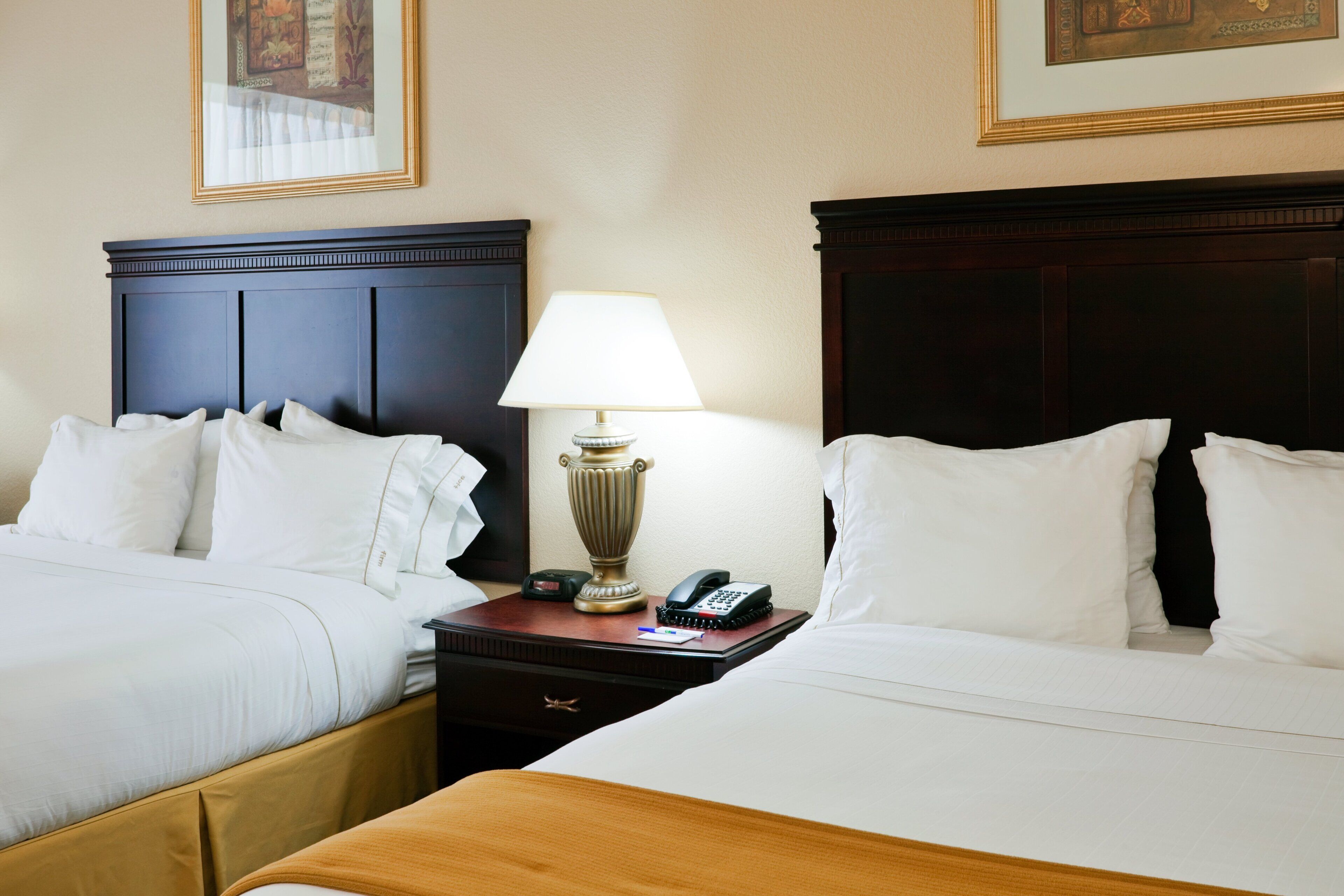 Quarto de hotel com duas camas, mesa de cabeceira com abajur, telefone e relógio.